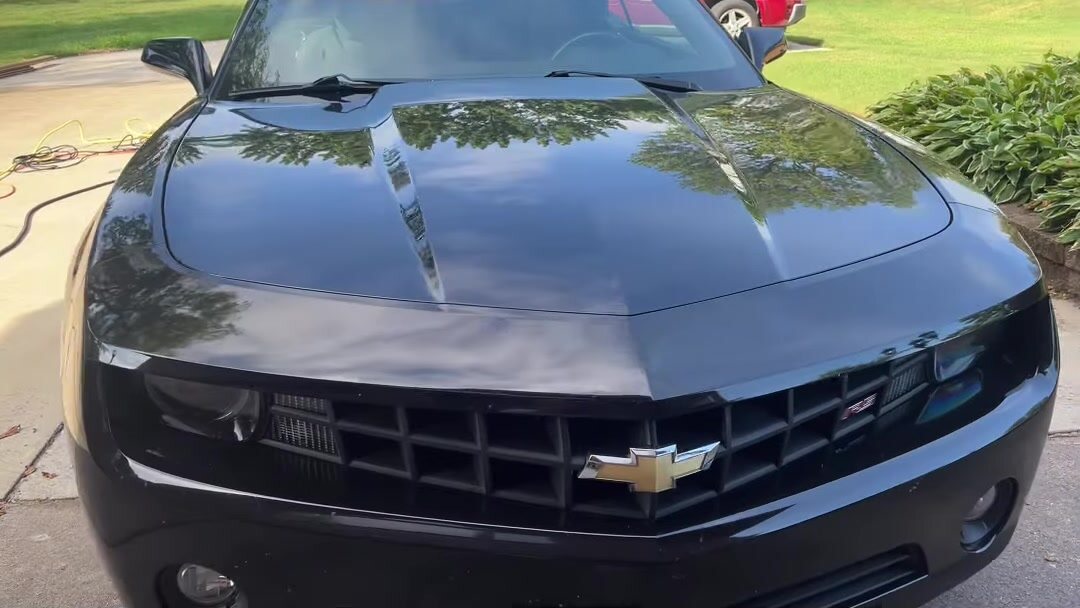 The same Camaro finished, gloss black hood reflecting the trees