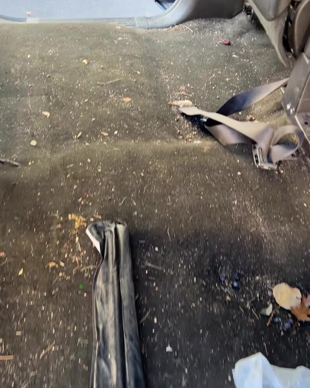 Rear floor of a car covered in dirt, leaves and debris before detailing